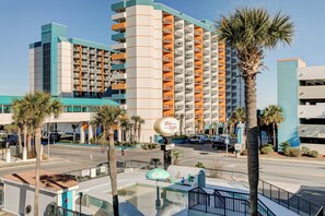 A multi-story hotel with balconies, a pool area with a children's play structure, and palm trees. - huuuùhhhhggg (Myrtle Beach)