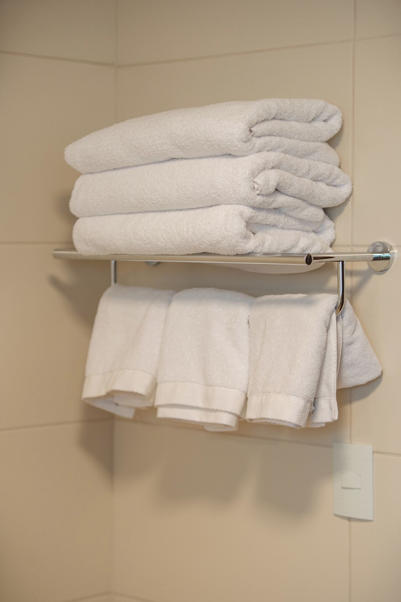 Casa de banho com um porta-toalhas com vários toalhos brancos dobrados com cuidado.