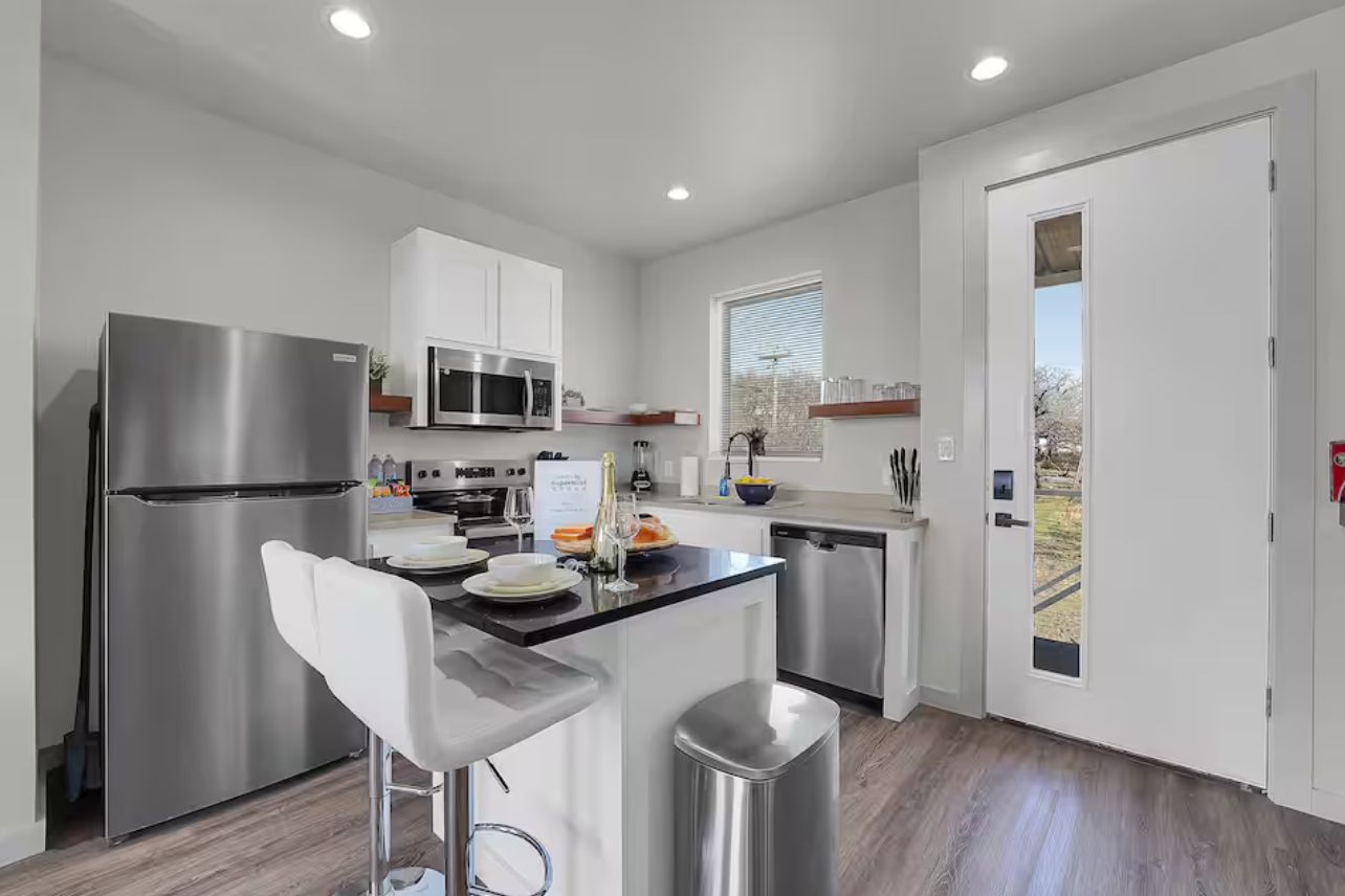 Una cocina moderna con electrodomésticos de acero inoxidable, un taburete de bar y vistas al exterior.