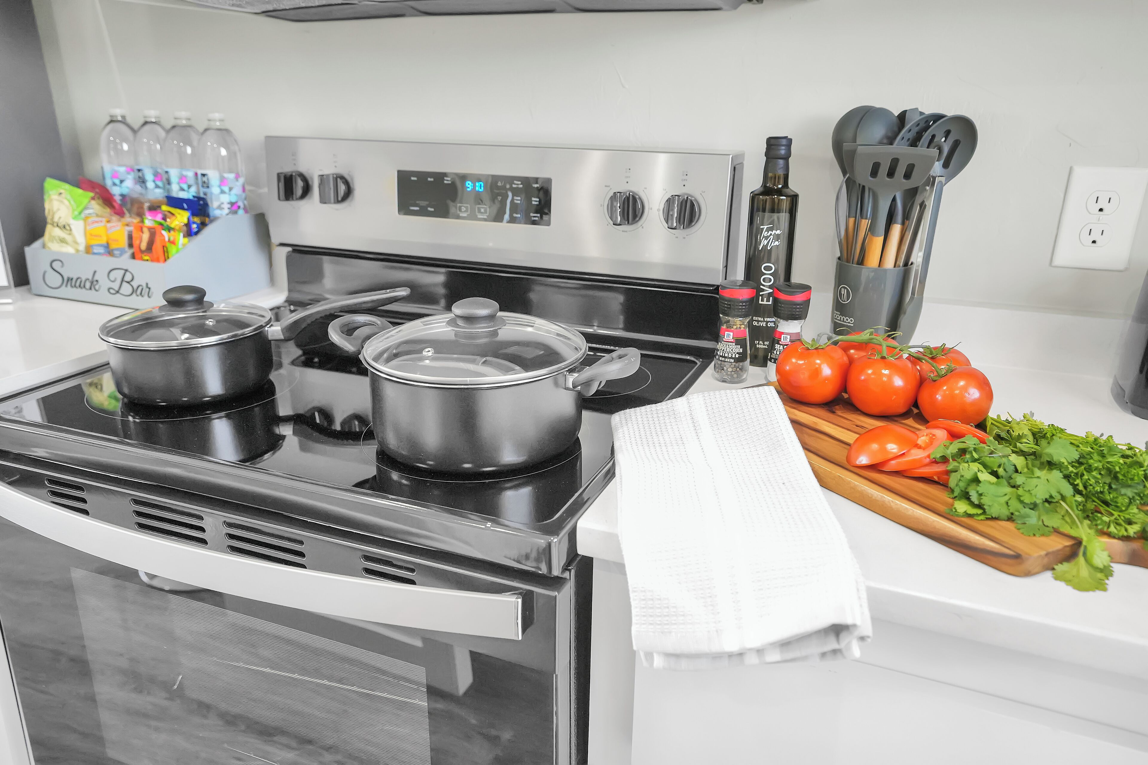 Una cocina con estufa, ollas, barra para aperitivos y tomates frescos con hierbas en la encimera.