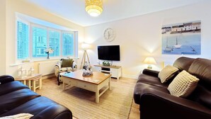 A living room with a wooden coffee table, two sofas, a TV, and a painting of a boat on the wall. - Paddy's Corner -  a cottage that sleeps 7 guests  in 3 bedrooms (Filey)