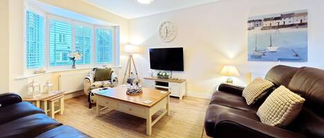 A living room with a wooden coffee table, two sofas, a TV, and a painting of a boat on the wall.