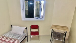 Una habitación pequeña y limpia con una cama, una silla y una mesita.
