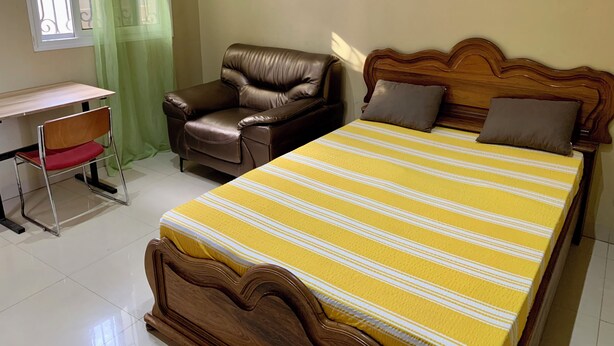 Un dormitorio con cama, una silla, un escritorio y una ventana con cortinas.