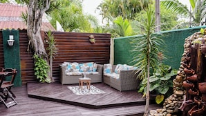 A wooden deck with outdoor furniture, surrounded by a green wall and tropical plants.