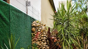 A wicker sofa with a tropical print cushion, a stone wall with plants, and a small palm tree.