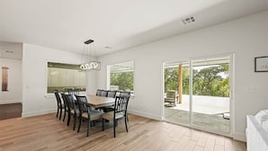 Un área de comedor con una mesa y sillas de madera, ventanas amplias y una puerta corrediza de vidrio que da a un patio exterior.
