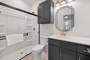 Et moderne badeværelse med en glasbrusekabine, et hvidt toilet og sorte skabe med guldgreb.