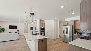 Una cocina moderna con una isla central, electrodomésticos de acero inoxidable y una lámpara colgante.