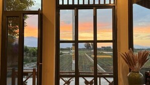 A room with a large window offering a view of a sunset over a landscape with fields and distant mountains. - Heyuan Hotel (Dali City)