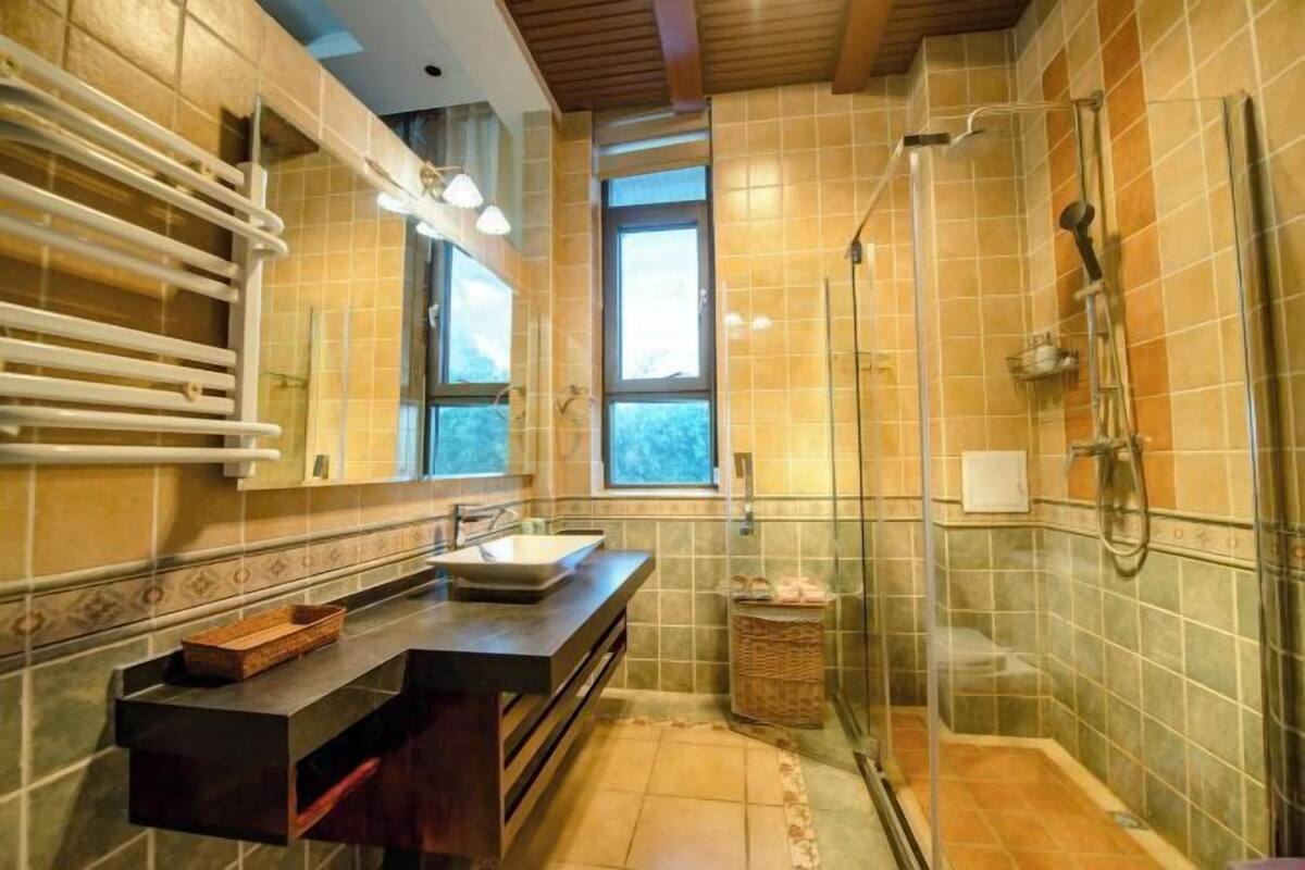 A modern bathroom with a large mirror, a sink, a shower, and a window providing natural light.