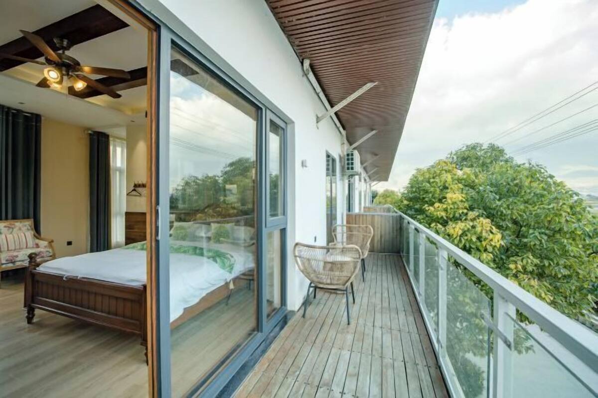 A balcony with a wooden floor, glass doors leading to a bedroom with a bed, and a chair.