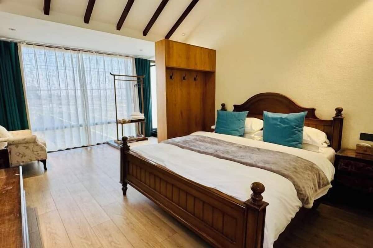 A bedroom with a wooden bed, a wooden wardrobe, a chair, and a large window with curtains.