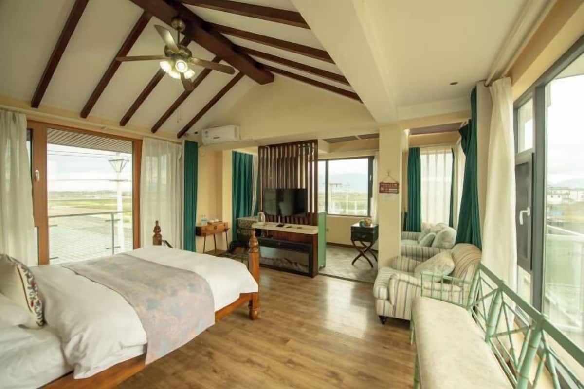 A spacious bedroom with a large bed, a desk, a sofa, and a balcony with a view.