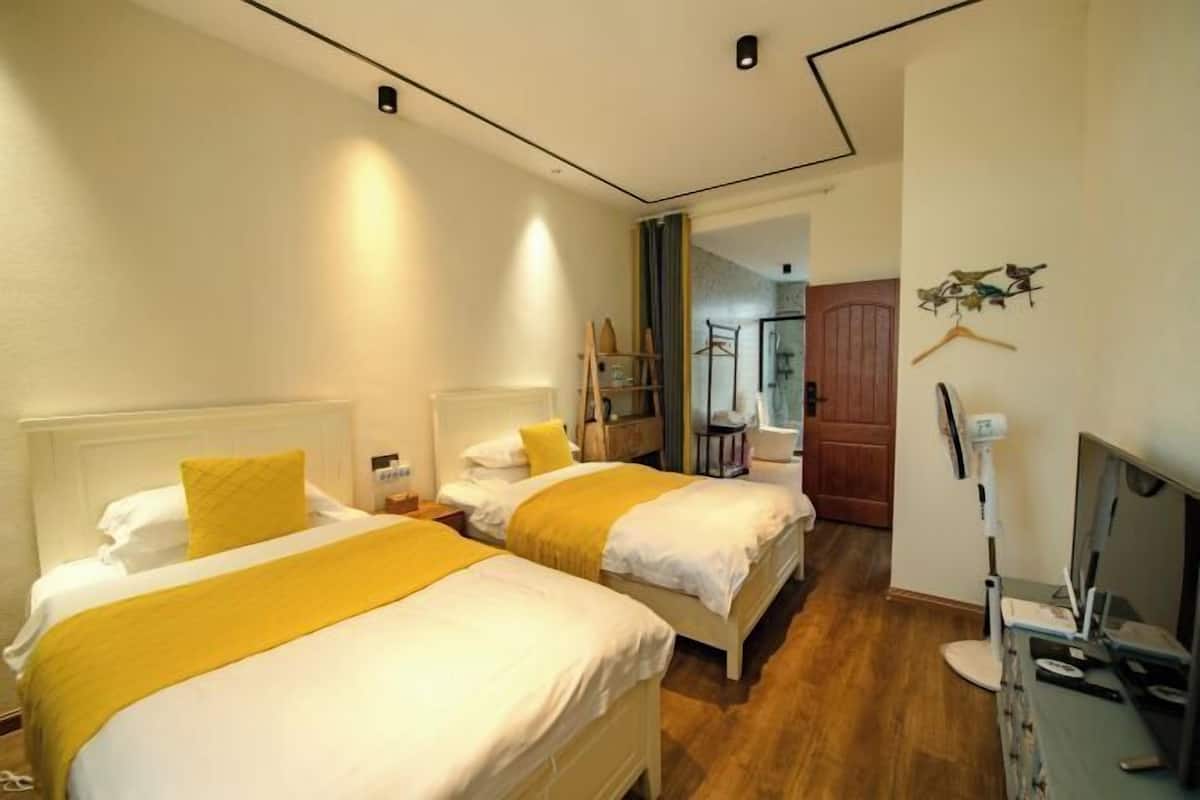 A hotel room with two beds, a TV, and a wooden floor.