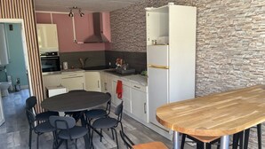 Eine kompakte Küche mit Essbereich, mit einer Wandverkleidung aus Stein, einem weißen Kühlschrank und einem runden Esstisch mit Stühlen.