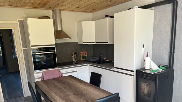 Eine kleine Küche mit Holztisch und -stühlen, einem eingebauten Backofen, einer Spüle und einem schwarzen Geräteblock.