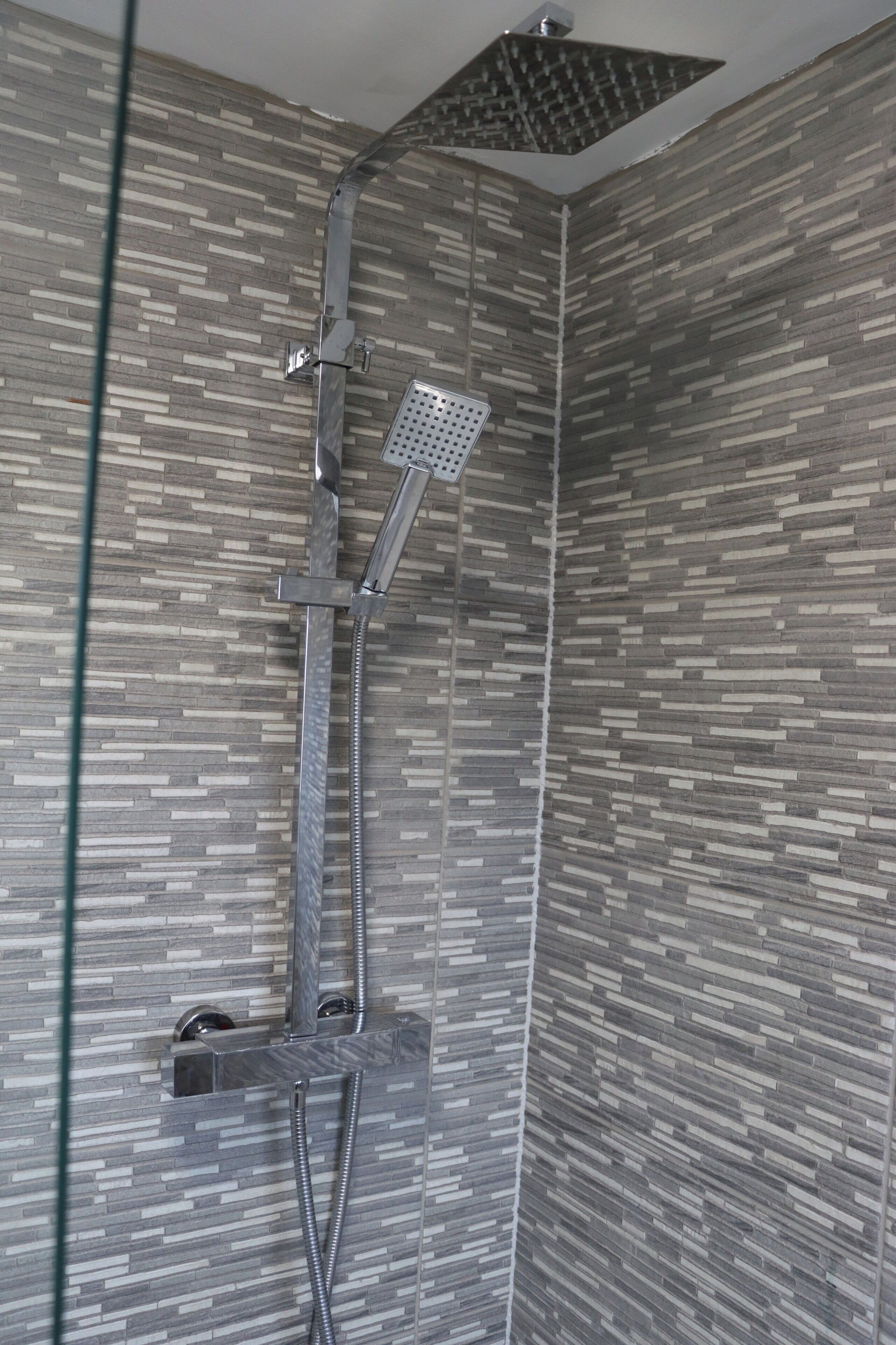 A shower with a rain showerhead and a handheld showerhead, mounted on a wall with a textured tile pattern.