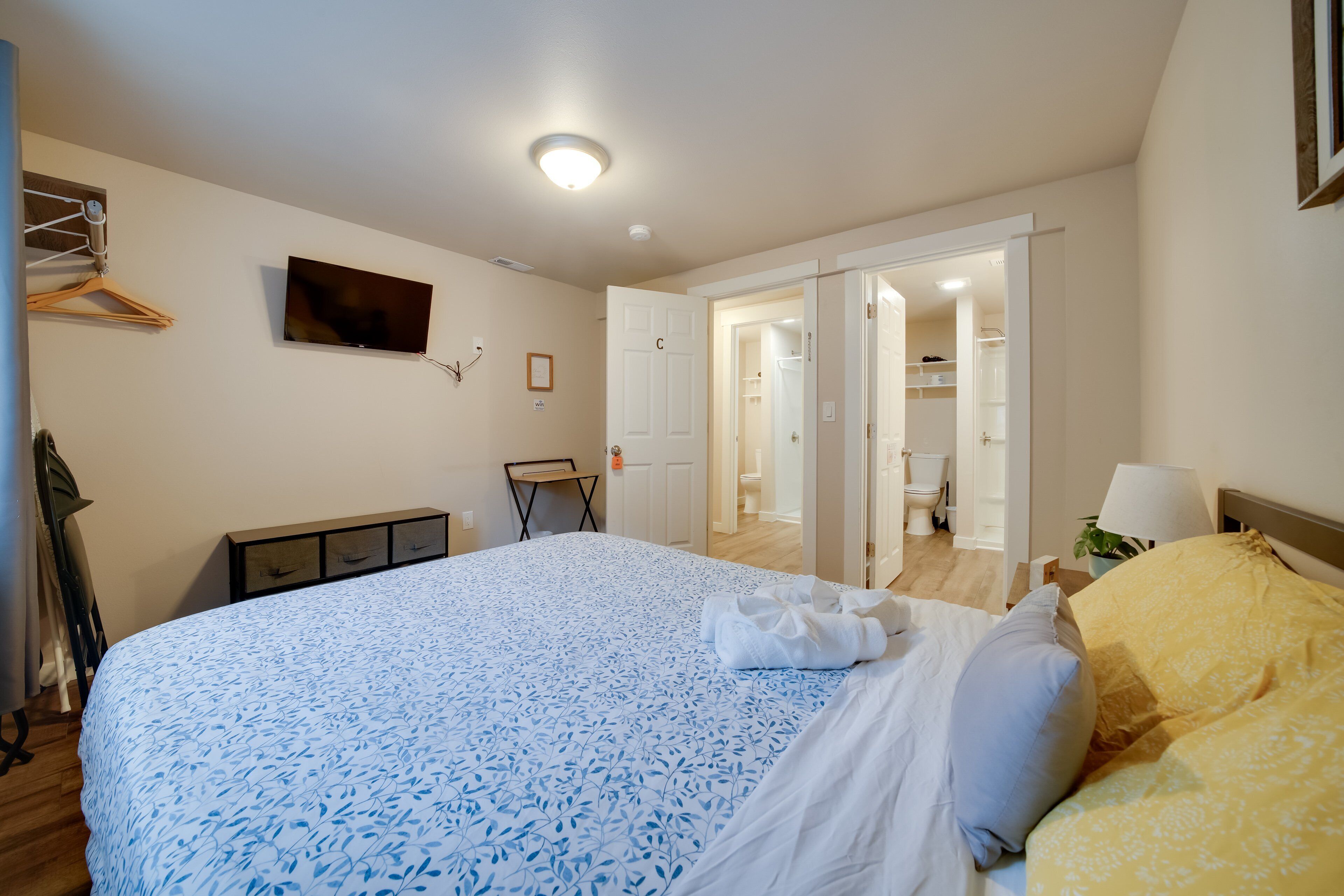 A bedroom with a bed, a TV, a wardrobe, and a bathroom visible through an open door.