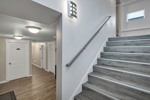 A staircase with a handrail, a light fixture on the wall, and a door at the bottom.