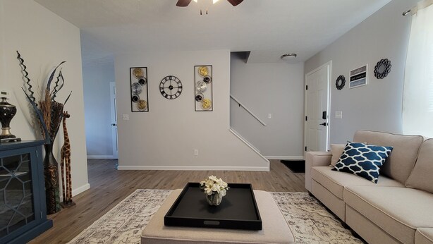 A living room with a sofa, a coffee table with a tray, a staircase, and wall decorations including clocks.