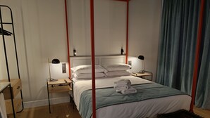 A bedroom with a four-poster bed, bedside tables, a desk, and a chair.