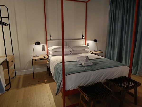 A bedroom with a four-poster bed, bedside tables, a desk, and a chair.