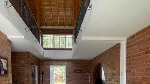 A spacious room with a high ceiling, brick walls, and a large window. There are two sofas and two armchairs arranged around a central table. - 2-story country farm in Guarne (Guarne)