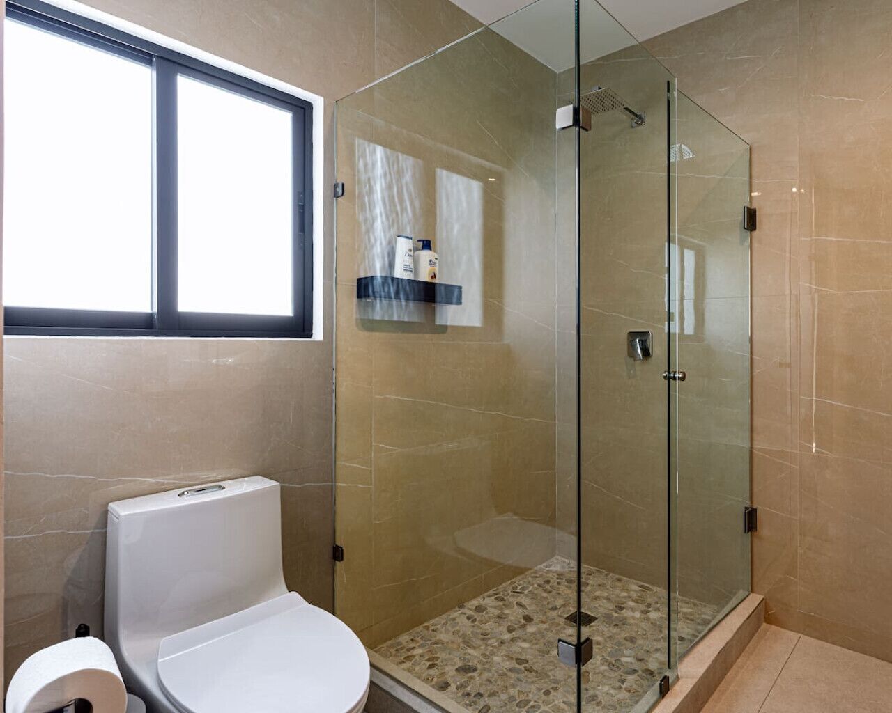 Et badeværelse med toilet, brusekabine i glas og et vindue.