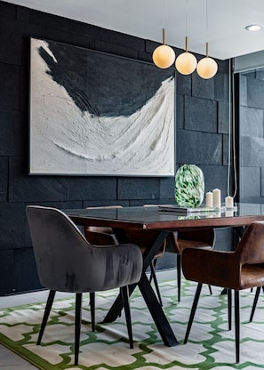 Un espace repas moderne avec un mur de couleur sombre, un grand tableau abstrait, une table à manger en bois et des chaises noires.