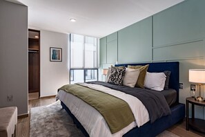 Cozy retreat with a large bed, bedside table, and lamp, set against a stylish wall panel.