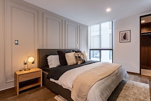 A modern bedroom with a large bed, bedside tables, a window, and a wardrobe.
