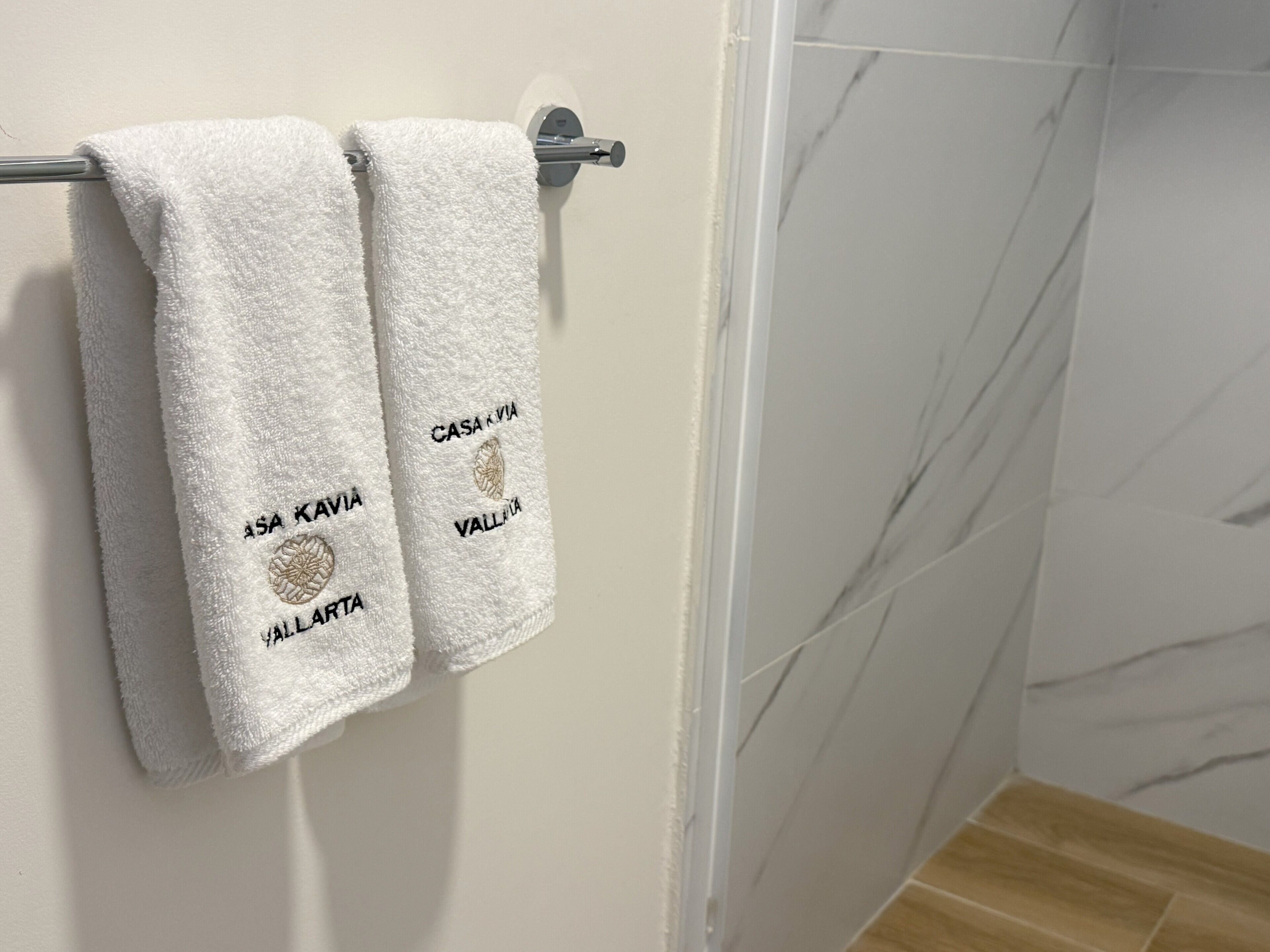 Two white towels hanging on a metal towel rack with embroidered text and a logo.