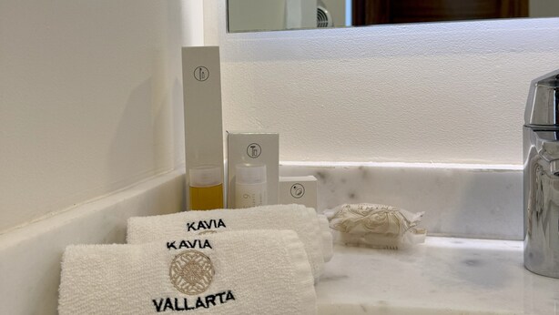 Un tocador de baño con encimera blanca, un espejo y un perchero con dos toallas que dicen 'KAVIA VALLARTA'.