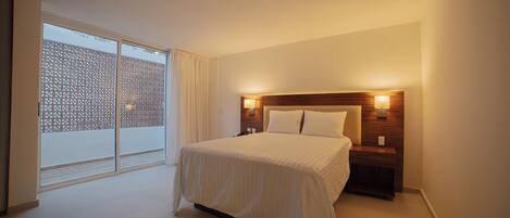 A hotel room with a large bed, a wooden headboard, bedside lamps, and a sliding glass door leading to an outdoor area.