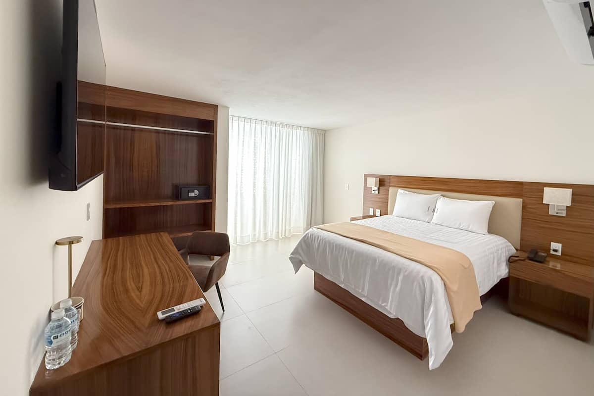 A hotel room with a bed, bedside tables, a desk with a chair, a TV mounted on the wall, and a wardrobe.