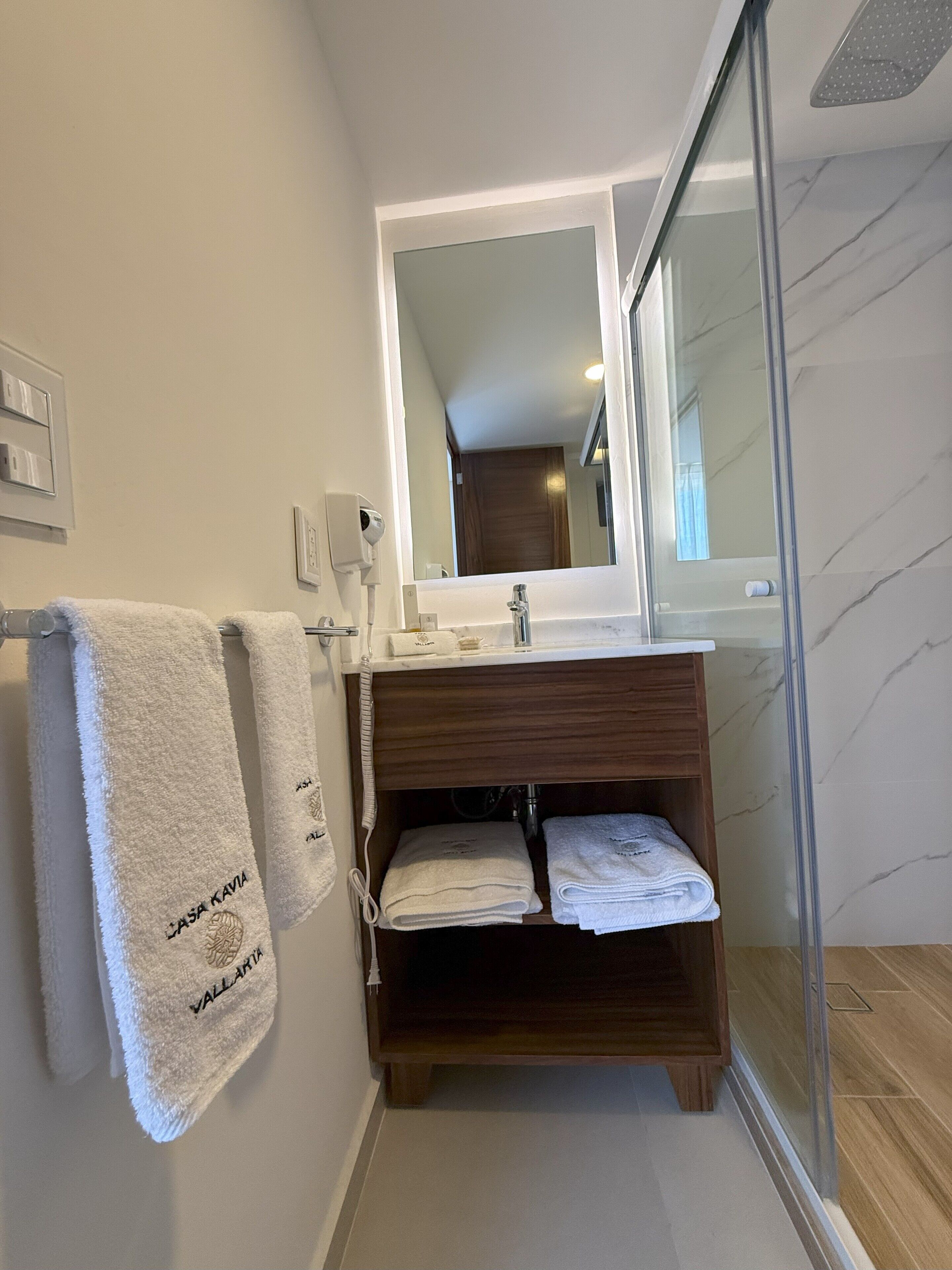 A bathroom with a wooden vanity, a mirror, and a glass shower enclosure.
