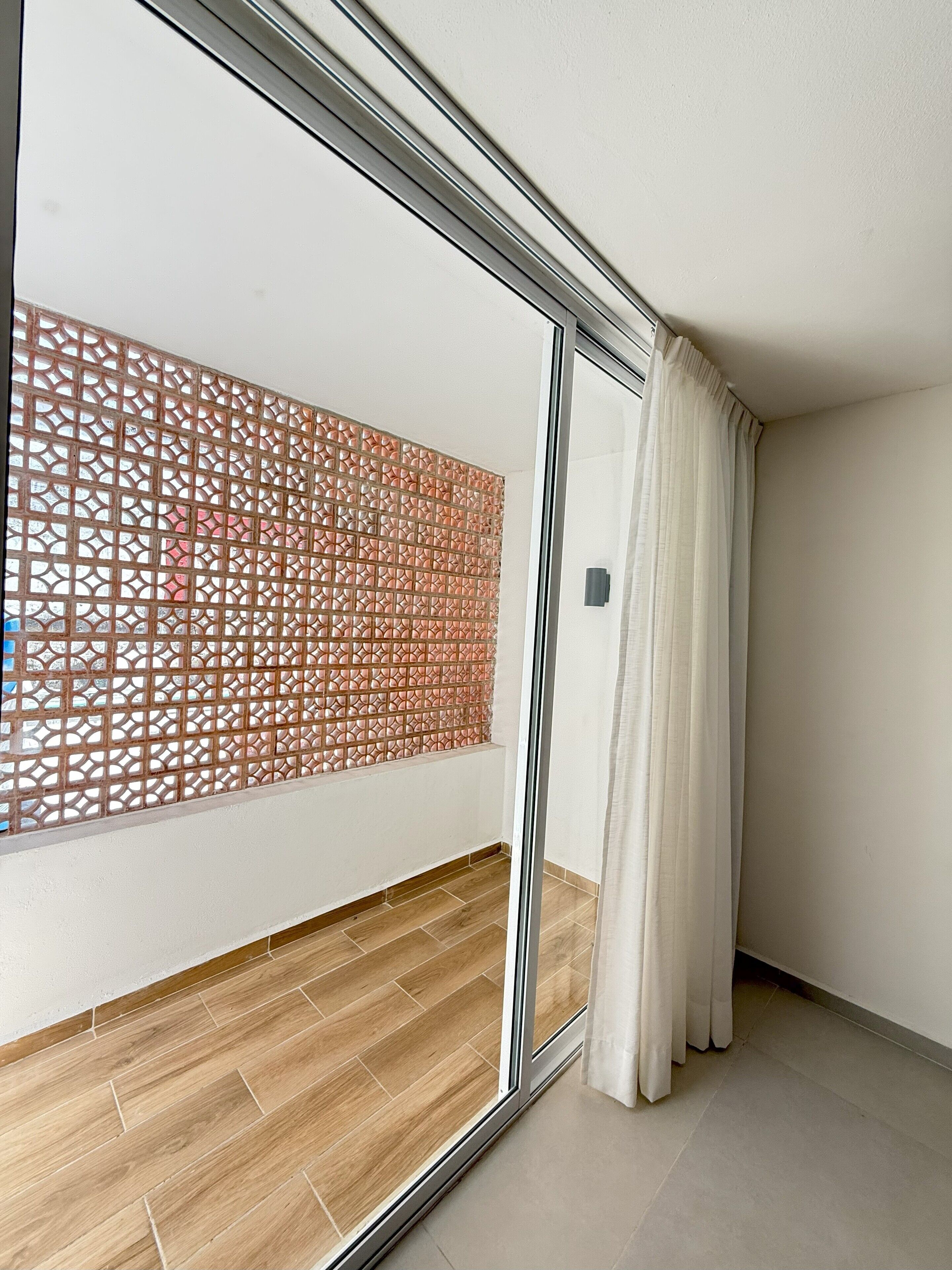 Una habitación con puerta corredera de vidrio, piso de madera y un separador decorativo.