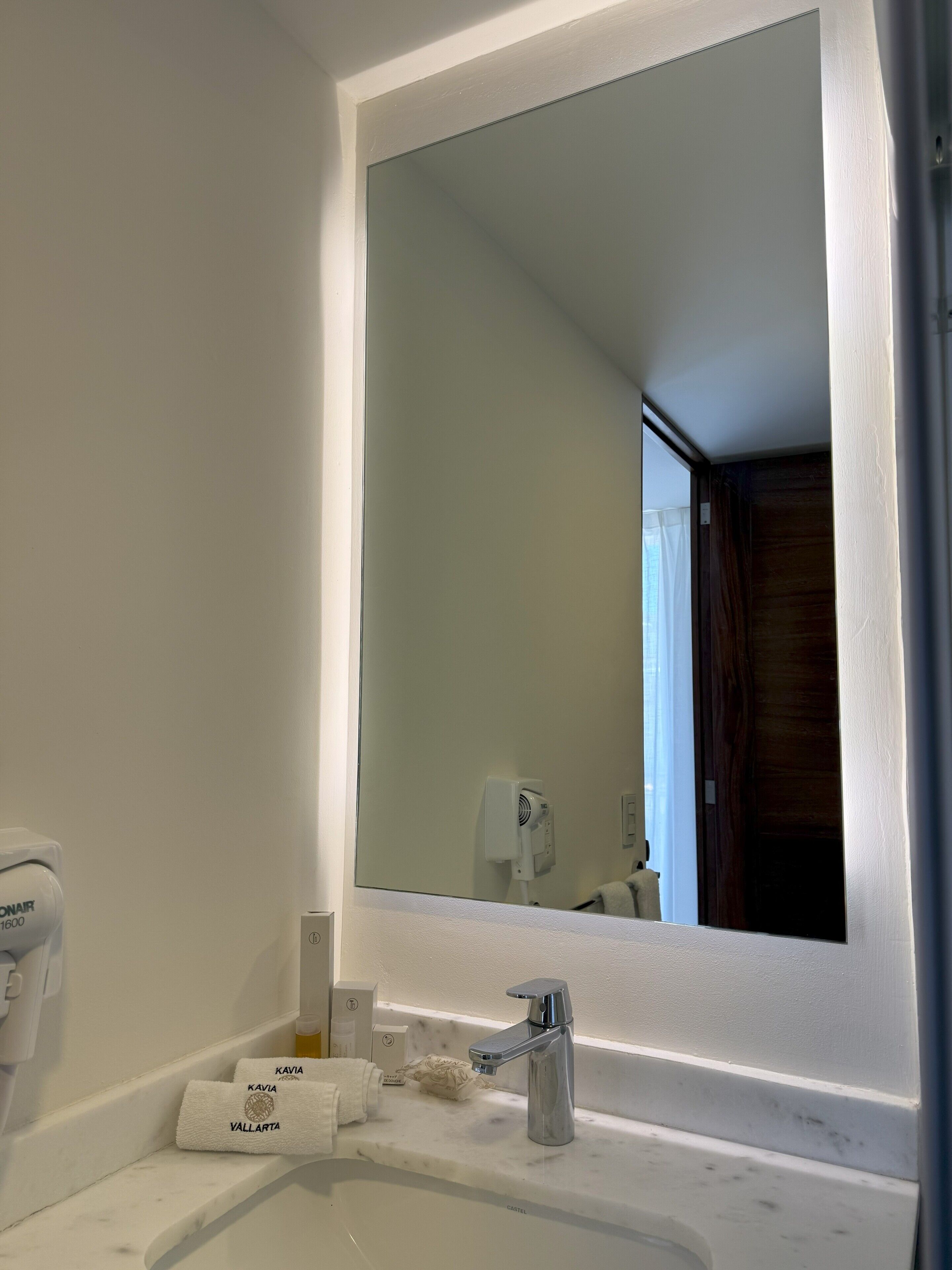 A bathroom with a white sink, a mirror, a handheld showerhead, and a towel rack with towels.