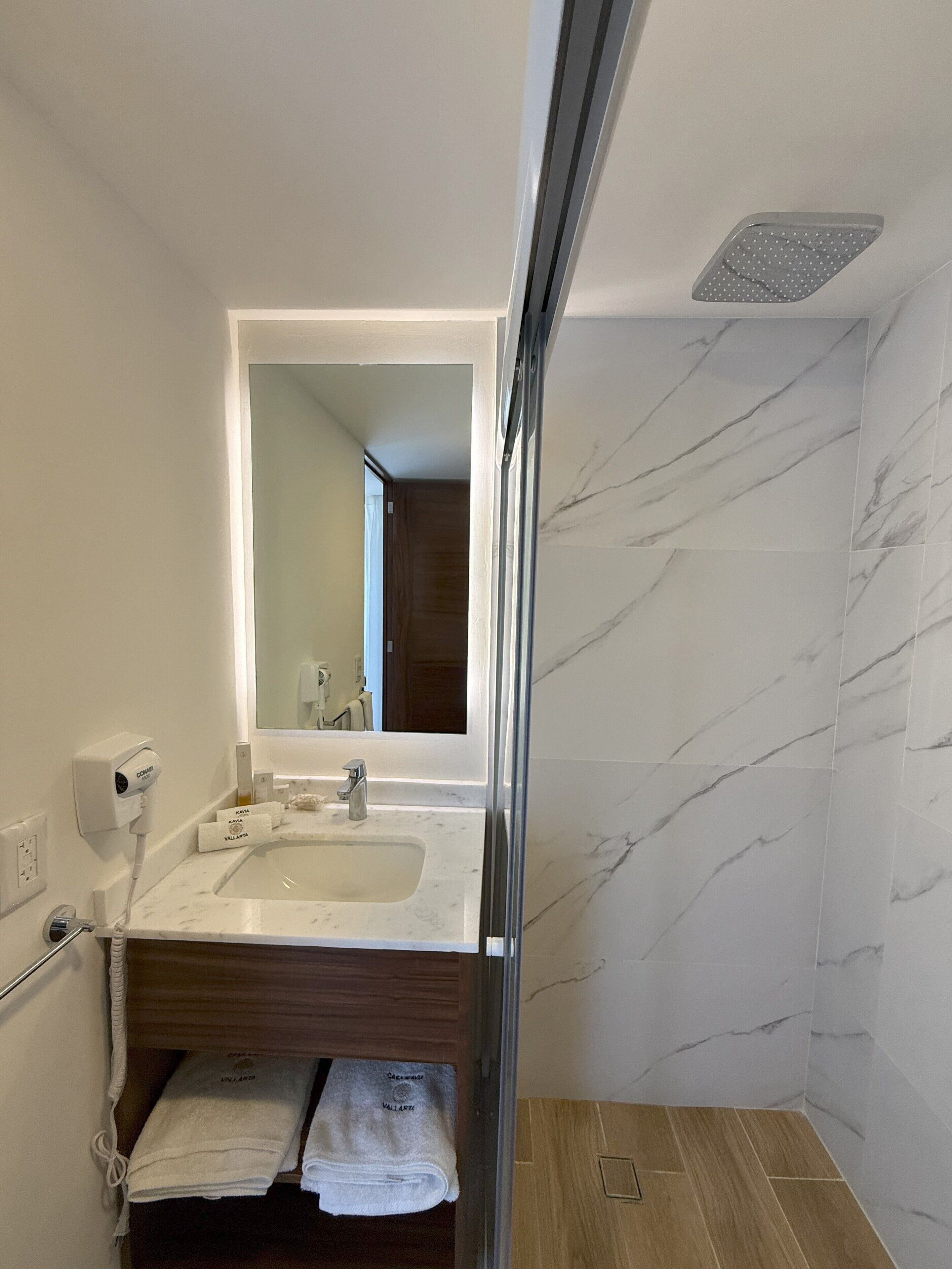 Un baño con lavamanos de mármol, espejo, ducha y toallero.