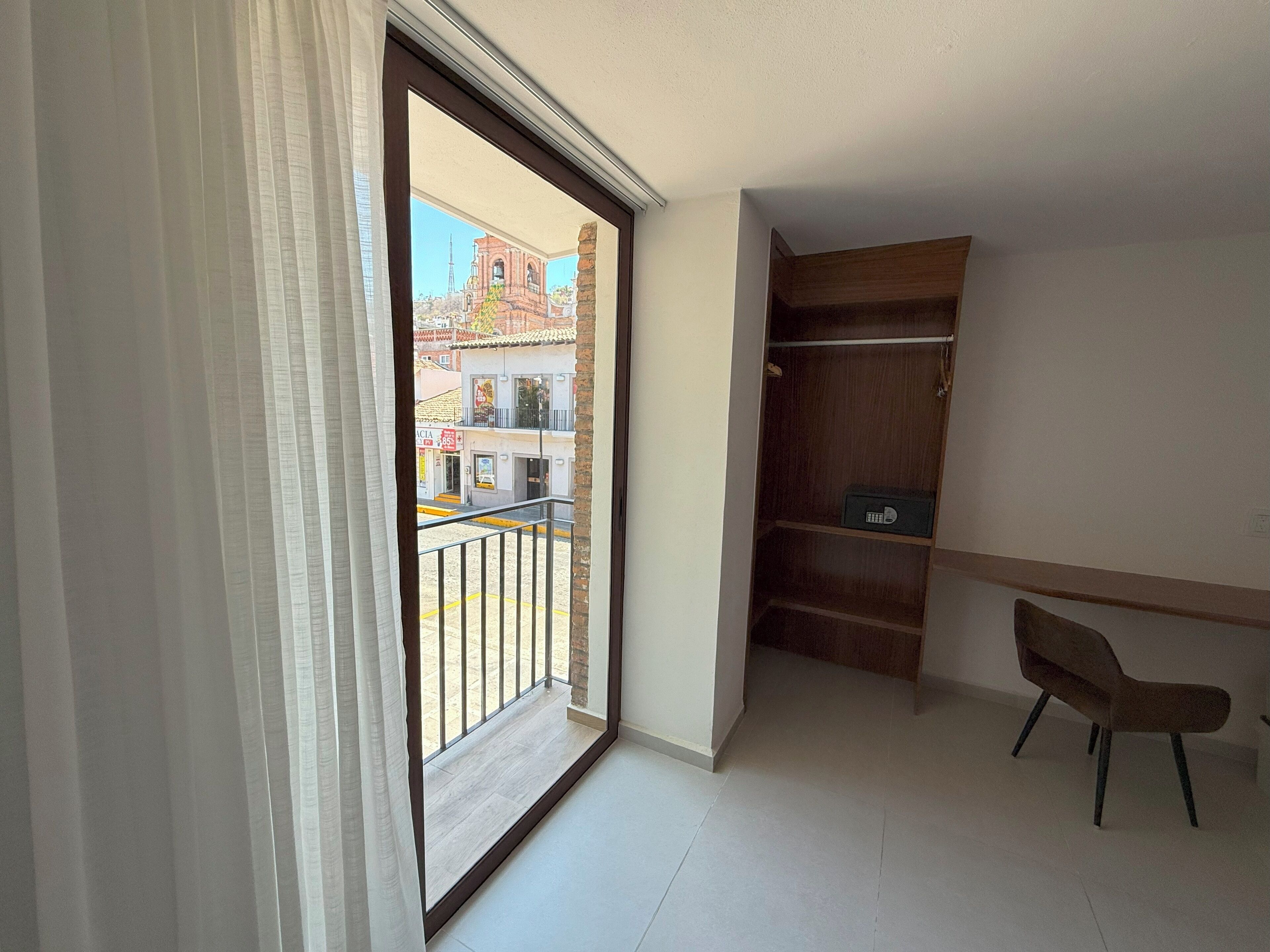 Un balcón con vistas a edificios y un armario de madera con una silla.