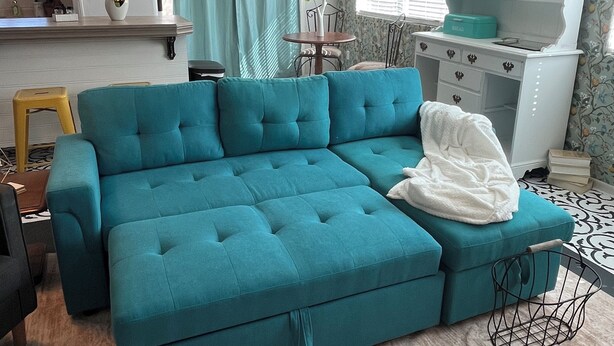 A teal sectional sofa in a living room with a kitchen area, a dining table, and a decorative shelf. - Single bedroom in a charming house in fabulous Phoenix with WiFi, AC, & more! (Phoenix)
