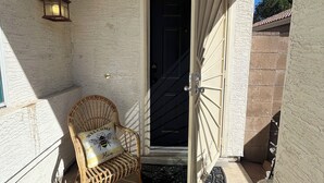 A porch with a wicker chair, a welcome pillow, a door, and a wall-mounted lantern. - Single bedroom in a charming house in fabulous Phoenix with WiFi, AC, & more! (Phoenix)
