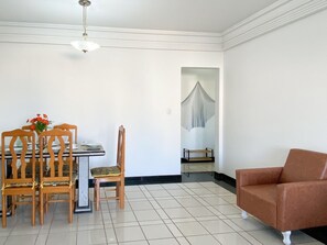 A dining area with a table, chairs, and a vase of flowers. There is a sofa in the corner and a hanging light fixture. - Ático con piscina - Guarapari (Guarapari)