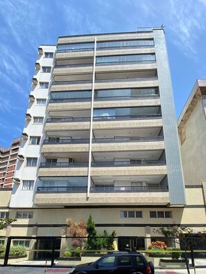 A multi-story building with a tiled facade, balconies on each floor, and a gated entrance with landscaping. - Ático con piscina - Guarapari (Guarapari)