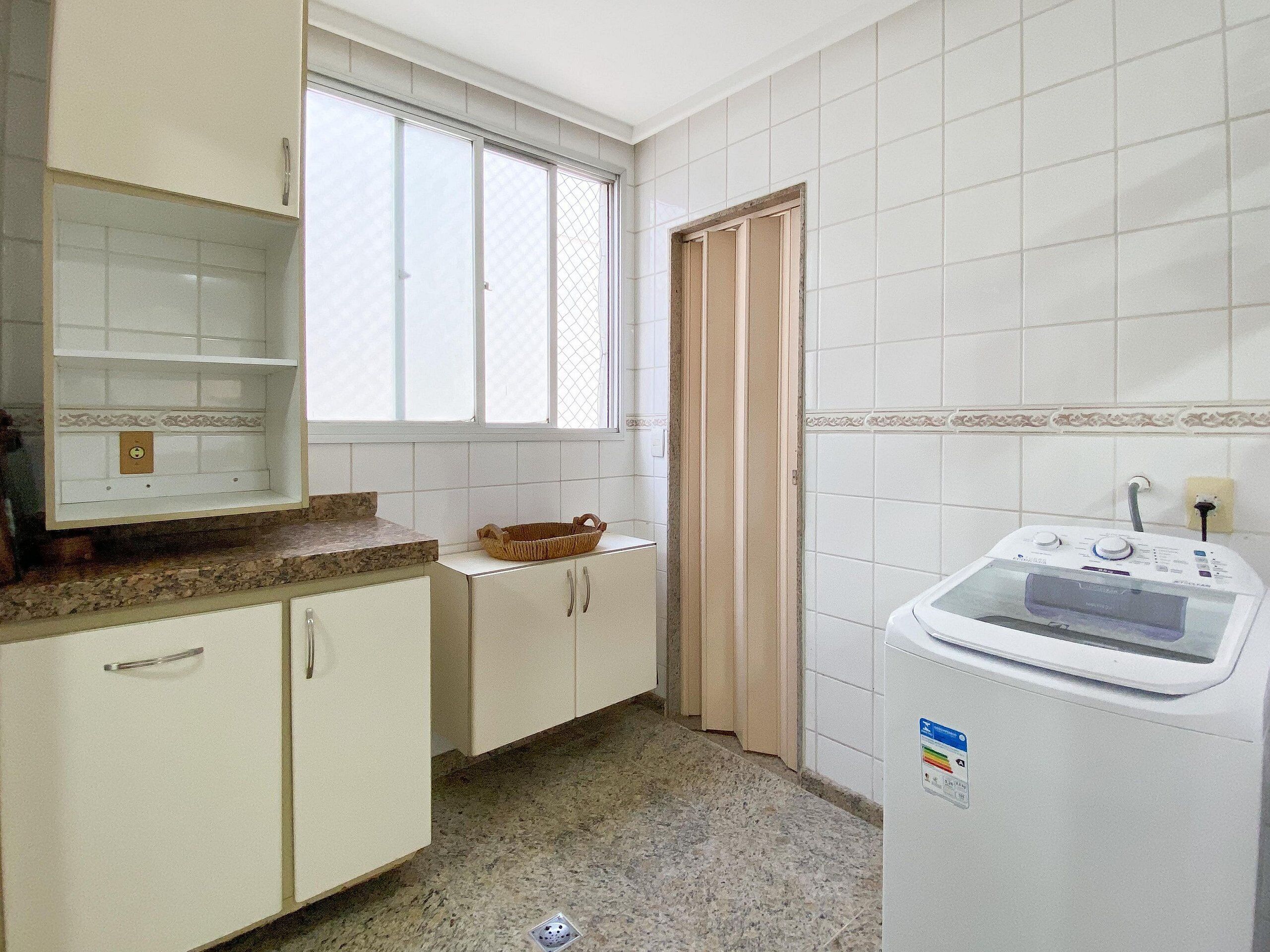 A kitchen with white cabinets, a granite countertop, a window with blinds, and a built-in washing machine.