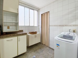 A kitchen with white cabinets, a granite countertop, a window with blinds, and a built-in washing machine. - Ático con piscina - Guarapari (Guarapari)