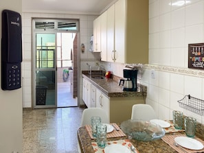 A kitchen with white cabinets, a coffee maker, and a dining area with plates and glasses. - Ático con piscina - Guarapari (Guarapari)