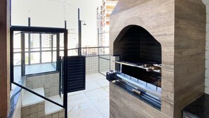 An outdoor kitchen area with a built-in oven, a sliding door, and a view of the cityscape. - Ático con piscina - Guarapari (Guarapari)
