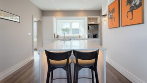 A modern kitchen with a central island, two bar stools, and artwork on the walls.